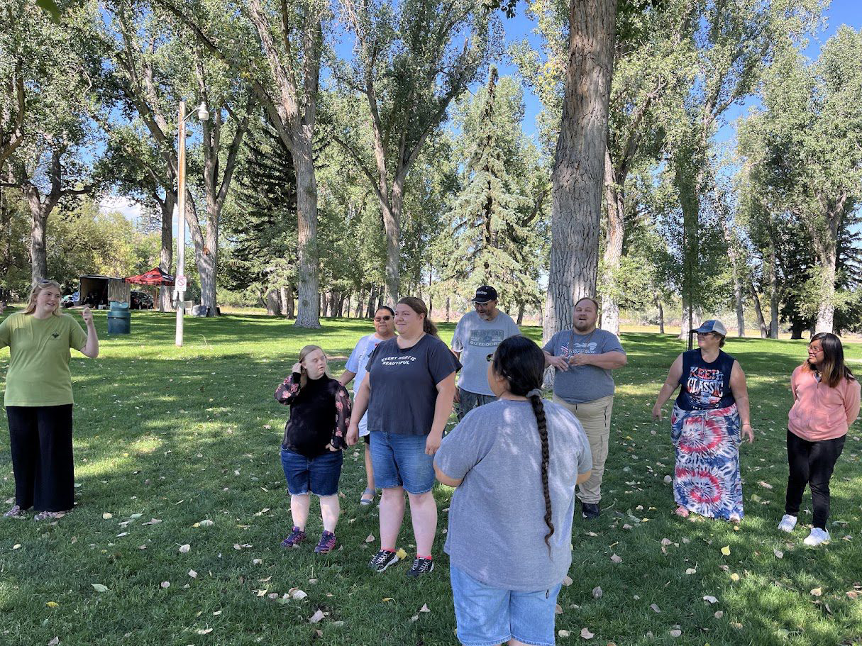 IMG_7357 (7) A group of people standing in a sunny park with trees and grass.